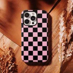 Peut inclure: Une coque de smartphone avec un motif à damier noir et rose clair. La coque présente une découpe rectangulaire dans le coin supérieur gauche pour un système de caméra à trois objectifs et un flash, avec des bords noirs autour de l'écran.