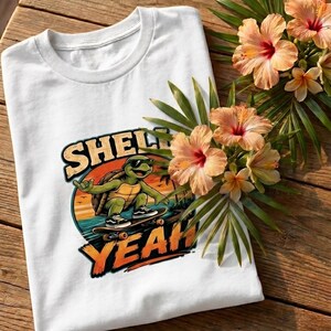 Könnte beinhalten: Ein weißes T-Shirt mit einer Grafik einer grünen Schildkröte mit Sonnenbrille auf einem Skateboard. Das Design zeigt einen Sonnenuntergang und den Text "SHELL YEAH!" in fetten orangefarbenen Buchstaben. Das T-Shirt liegt auf einer Holzoberfläche.
