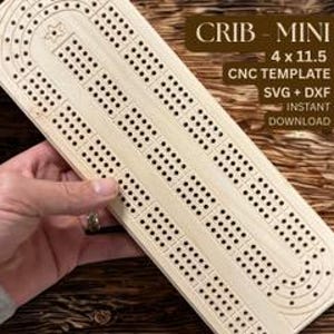 May include: A light-colored wooden cribbage board with drilled holes for pegs. The board is rectangular, with a star-shaped design at one end. Text on the board reads "CRIB - MINI 4 x 11.5 CNC TEMPLATE SVG + DXF INSTANT DOWNLOAD". The board is 4 inches wide and 11.5 inches long.