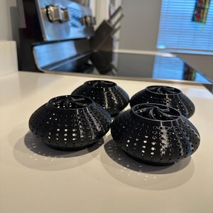May include: Four black, spherical decorative objects with a perforated design. They are arranged on a white countertop. The objects have a unique, textured appearance, and are likely 3D printed.