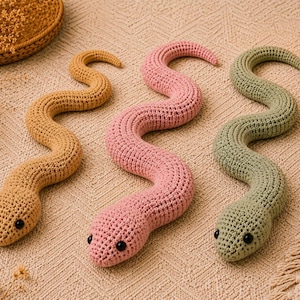 Pode incluir: Três cobras feitas à mão em crochê nas cores amarelo mostarda, rosa suave e verde sálvia. Cada brinquedo de pelúcia apresenta um corpo longo e sinuoso com uma superfície de fio texturizado e duas pequenas contas pretas redondas como olhos.