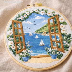 May include: Embroidered artwork in a wooden hoop depicts a coastal scene. A window frame opens onto a blue sea with sailboats, a green island, and a blue sky with clouds. White flowers and blue flower pots frame the window.