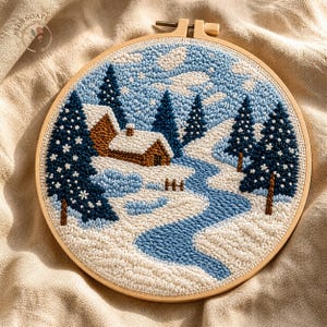 Könnte beinhalten: Handgesticktes Winterlandschaftsbild in einem Holzrahmen. Das Design zeigt ein Haus, einen Fluss und Bäume in Blau-, Weiß- und Brauntönen. Die Stickerei zeigt eine verschneite Landschaft mit einem sich schlängelnden Fluss.
