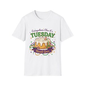 May include: White t-shirt featuring a colorful Mardi Gras design. The graphic includes a cake, beads, and the text "Everywhere Else it's Tuesday" and "Mardi Gras". The design is in shades of green, purple, yellow, and white.