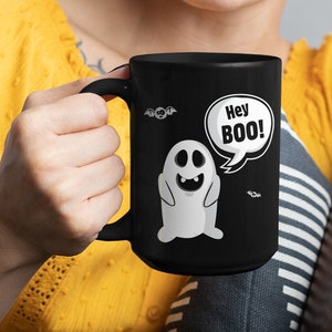 May include: A black coffee mug with a white ghost graphic and the text "Hey BOO!" in a speech bubble. The ghost has a toothy grin and is surrounded by bats.