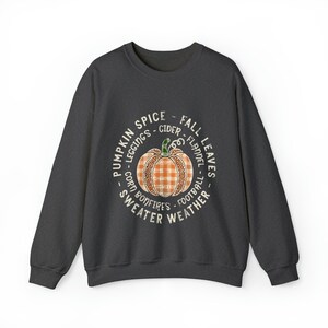 May include: A dark grey sweatshirt with a white circle graphic featuring a pumpkin with a plaid pattern and the text "Pumpkin Spice - Fall Leaves - Leggings - Cider - Flannel - Corn - Bonfires - Football - Sweater Weather".