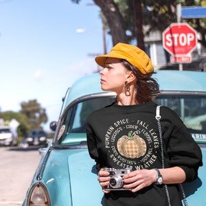 May include: Black sweatshirt with a pumpkin spice themed graphic. The graphic features a pumpkin with a plaid pattern and text that reads "Pumpkin Spice - Leggings - Cider - Fall - Flannel - Corn Bonfires - Football - Sweater Weather - Fall Leaves".