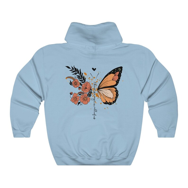 May include: Light blue hoodie featuring a butterfly design. The butterfly is orange and black, with floral and leaf accents. The text "there is magic in all of us" is written vertically on the right side of the butterfly. The hoodie has a drawstring hood.