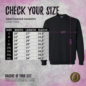 May include: Size chart for an adult crewneck sweatshirt. The chart shows the size, width, length, and sleeve length in inches. The chart is on a pink background with a black sweatshirt in the background.