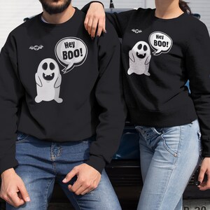 May include: A black sweatshirt with a white ghost graphic and the text "Hey Boo!" printed on it. The sweatshirt is being worn by a person.