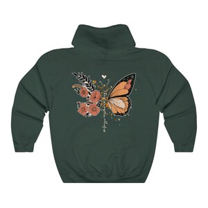 May include: A dark green hooded sweatshirt featuring a butterfly and floral design on the back. The butterfly is orange and black, with peach-colored flowers and the text "there is magic in all of us".