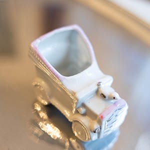 Peut inclure: Petite voiture en céramique blanche avec des détails roses. Le véhicule miniature présente des détails, notamment des phares et une calandre. Il s'agit probablement d'un objet décoratif ou d'un petit contenant.