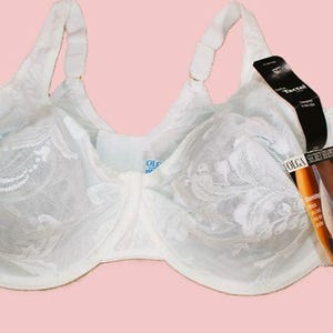 Könnte beinhalten: Ein weißer Bügel-BH mit einem transparenten floralen Spitzenüberzug auf den Körbchen und verstellbaren Trägern. Ein schwarzes Produktetikett ist am rechten Träger befestigt und zeigt den Text Olga Secret Shaper sowie Tactel.