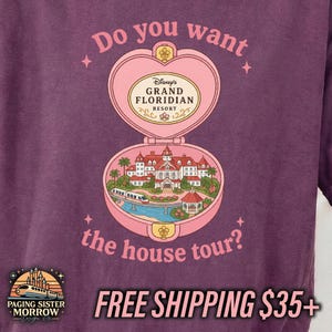 Puede incluir: Una camiseta de color morado oscuro con un gr&aacute;fico de un relicario rosa en forma de coraz&oacute;n. Dentro hay una ilustraci&oacute;n del Grand Floridian Resort con un monorra&iacute;l. El texto dice: Do you want the house tour? y Grand Floridian Resort.