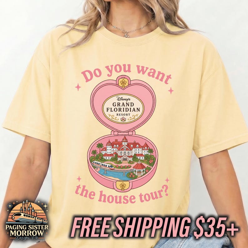 Puede incluir: Una camiseta de manga corta de color amarillo p&aacute;lido con un gr&aacute;fico de polvera rosa en forma de coraz&oacute;n. El dise&ntilde;o incluye el texto "Do you want the house tour?" y una ilustraci&oacute;n del Disney Grand Floridian Resort con un monorra&iacute;l y palmeras.