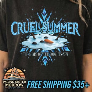 May include: Dark gray t-shirt with a blue graphic that says "CRUEL SUMMER" above a snowman scene. The design includes a snowflake and the text "THE SHAPE OF YOUR BODY, IT'S NEW".