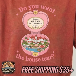 Puede incluir: Una camiseta color rojo ladrillo con un gr&aacute;fico de un estuche compacto rosa en forma de coraz&oacute;n. Dentro hay una ilustraci&oacute;n del Disney Grand Floridian Resort con un monorra&iacute;l. El texto dice: Do you want the house tour? y Disney's Grand Floridian Resort.