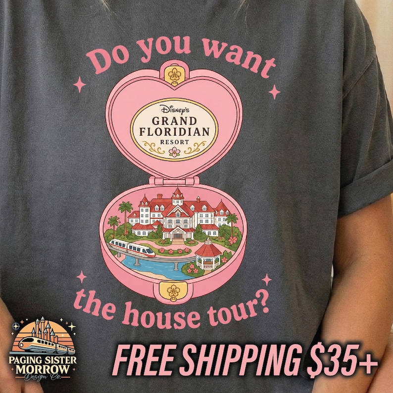 Puede incluir: Una camiseta gris carb&oacute;n con un gr&aacute;fico de un estuche compacto rosa en forma de coraz&oacute;n. Dentro hay una ilustraci&oacute;n del Disney Grand Floridian Resort con un monorra&iacute;l. El texto dice: Do you want the house tour? y Disney's Grand Floridian Resort.