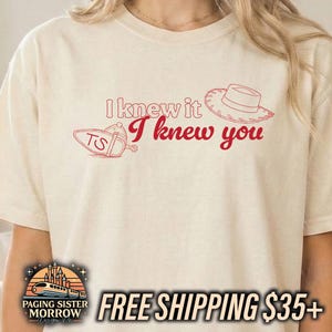 May include: A cream-colored short-sleeve t-shirt featuring red line art graphics. The design includes a cowboy hat, a cowboy boot with the letters TS, and the red text I knew it I knew you printed in a combination of outline and script fonts.