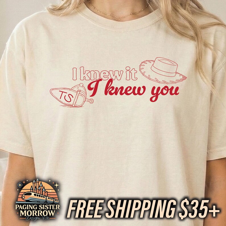 May include: A cream-colored short-sleeve t-shirt featuring red line art graphics. The design includes a cowboy hat, a cowboy boot with the letters TS, and the red text I knew it I knew you printed in a combination of outline and script fonts.