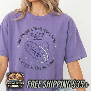 May include: A purple short-sleeve t-shirt featuring a graphic of a space ranger helmet and the text, but I've got a blank space, baby, and I'll write your name, with the name TAYLOR printed on the helmet and a Star Command logo above it.