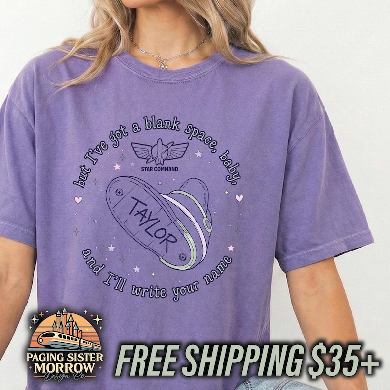 May include: A purple short-sleeve t-shirt featuring a graphic of a space ranger helmet and the text, but I've got a blank space, baby, and I'll write your name, with the name TAYLOR printed on the helmet and a Star Command logo above it.
