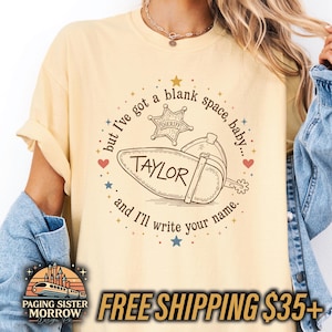 Peut inclure: Un t-shirt jaune p&acirc;le arborant un motif circulaire avec une &eacute;toile de sh&eacute;rif, une botte de cow-boy et le texte : but I've got a blank space, baby... TAYLOR and I'll write your name. Le design inclut de petites &eacute;toiles et c&oelig;urs color&eacute;s.
