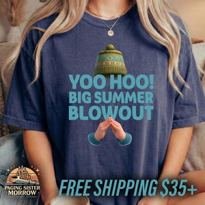May include: Navy blue t-shirt with the text "YOO HOO! BIG SUMMER BLOWOUT" in turquoise. The shirt features a green hat graphic and cartoon hands. The shirt is from Paging Sister Morrow Design Co.