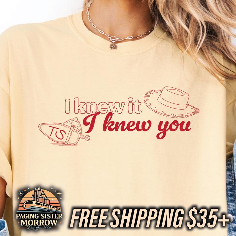 May include: A pale yellow t-shirt featuring the red text I knew it I knew you. The design includes a red outline of a cowboy hat and a spur with the letters TS. The shirt has a crew neckline and a relaxed fit, showcasing a graphic print.