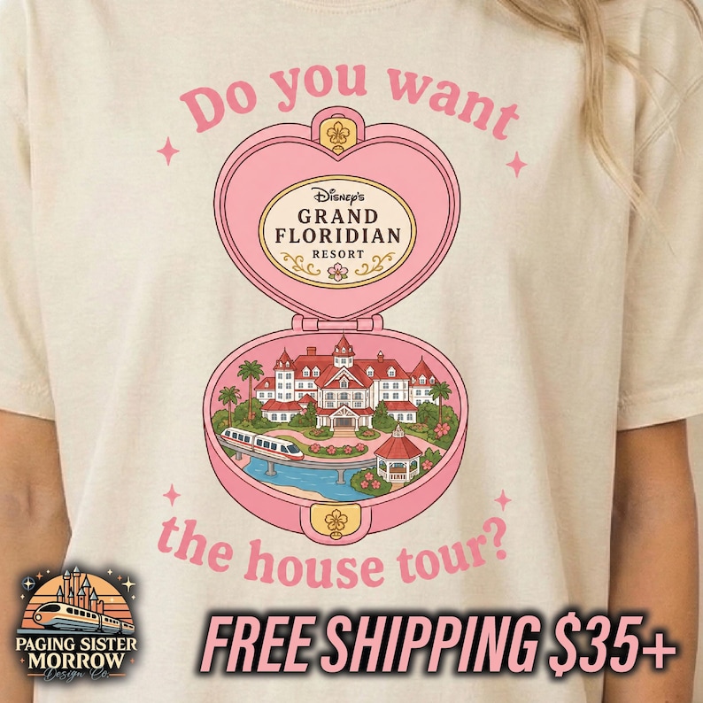 Puede incluir: Una camiseta beige con un gr&aacute;fico de un estuche rosa en forma de coraz&oacute;n. La parte superior muestra el texto "Do you want" y "Disney's GRAND FLORIDIAN RESORT". La parte inferior ilustra el complejo hotelero, un monorra&iacute;l y "the house tour?"