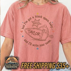 Peut inclure: Un t-shirt corail avec un motif marron repr&eacute;sentant un &eacute;peron de botte de cow-boy et une &eacute;toile de sh&eacute;rif. Le texte indique, but I've got a blank space, baby... and I'll write your name. Le nom TAYLOR est inscrit sur l'&eacute;peron en marron.