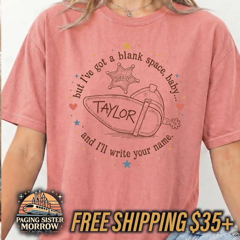 Peut inclure: Un t-shirt corail avec un motif marron repr&eacute;sentant un &eacute;peron de botte de cow-boy et une &eacute;toile de sh&eacute;rif. Le texte indique, but I've got a blank space, baby... and I'll write your name. Le nom TAYLOR est inscrit sur l'&eacute;peron en marron.