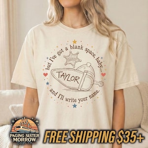 Peut inclure: Un t-shirt &agrave; manches courtes de couleur cr&egrave;me avec une impression graphique marron. Le motif comprend une &eacute;toile de sh&eacute;rif, une botte de cow-boy et le texte : but I've got a blank space, baby... TAYLOR and I'll write your name. Des &eacute;toiles et des c&oelig;urs entourent le texte.
