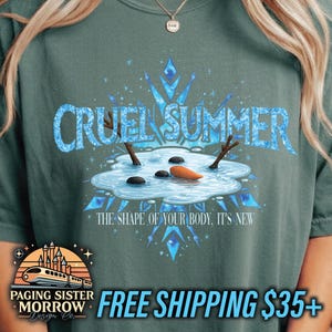 May include: A teal-colored t-shirt with the words "CRUEL SUMMER" in a light blue, icy font. The graphic features a melting snowman with a carrot nose and stick arms. The text "THE SHAPE OF YOUR BODY, IT'S NEW" is below the snowman.