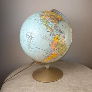 May include: A World Vision Series globe featuring a light blue ocean and multicolored continents. The globe is mounted on a circular gold-toned metal base with a matching meridian arc. Text on the globe includes World Vision Series.