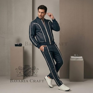 May include: Navy blue leather tracksuit with white piping. The jacket has a zip-up front and the trousers have a straight leg design. The outfit is paired with white trainers. The brand name "Bavaria Craft" is visible.