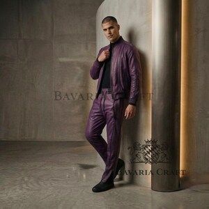 May include: A two-piece purple leather outfit, consisting of a bomber jacket and matching pants. The jacket has a black collar and cuffs. The pants have a vertical seam down the front of each leg. The outfit is worn with a black top and shoes.