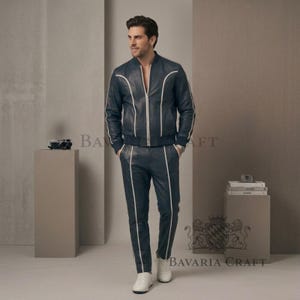 May include: Navy blue leather bomber jacket and matching trousers with white piping. The jacket features a zip closure, and the trousers have a straight leg. The outfit is completed with white trainers.