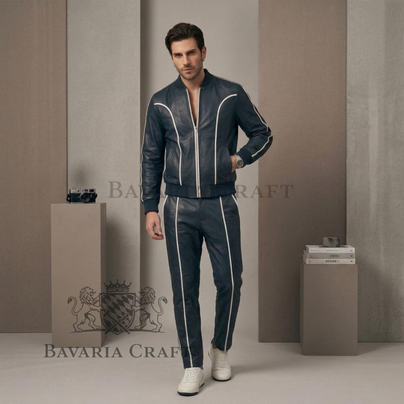 May include: Navy blue leather bomber jacket and matching trousers with white piping. The jacket features a zip closure, and the trousers have a straight leg. The outfit is completed with white trainers. The text "BAVARIA CRAFT" is visible.