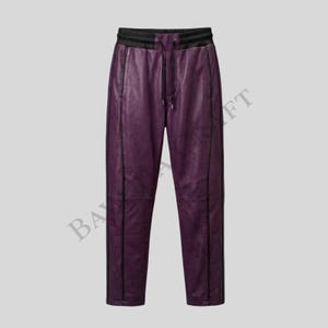 May include: Purple leather pants with black trim and a drawstring waist. The pants have a relaxed fit and a subtle sheen. The design includes vertical seams down the front and back of the legs. The waistband is black.