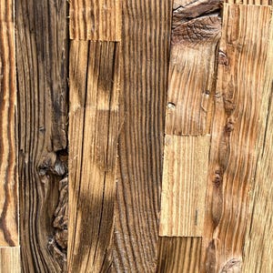 Peut inclure: Gros plan sur une surface en bois composée de planches verticales de différentes nuances de brun et de beige. Le grain du bois est visible, avec des nœuds et des textures, créant une esthétique rustique et naturelle. Les planches sont disposées en quinconce.