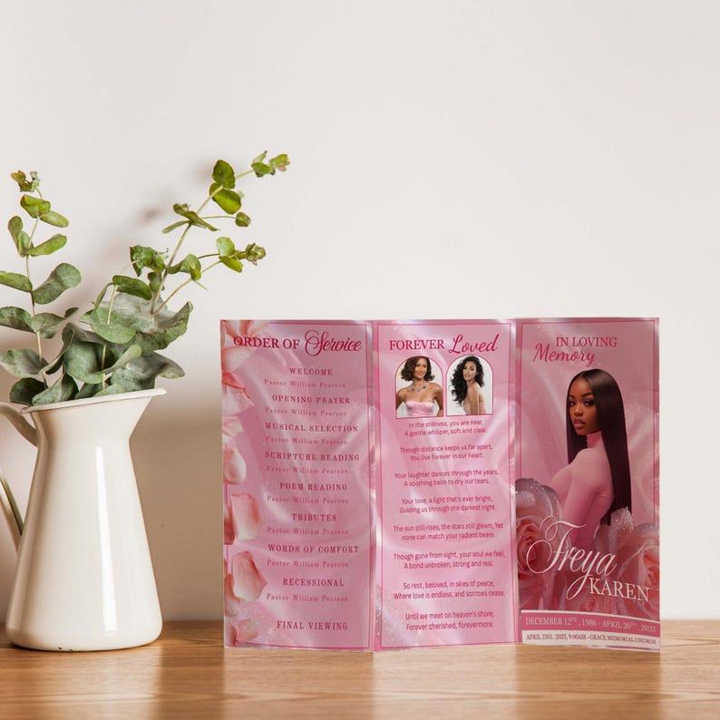 May include: A pink memorial service program, featuring the text "Order of Service," "Forever Loved," and "In Loving Memory." The program includes photos and text, with a floral design. The program is displayed on a wooden surface.