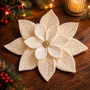 May include: A cream-colored crocheted poinsettia flower ornament featuring layered, pointed petals with a textured stitch pattern and a small, round, metallic gold center. The flower is shaped like a star with multiple overlapping petal layers.