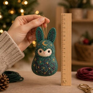 May include: A teal crochet rabbit ornament featuring a gold embroidered crescent moon on the forehead and gold star patterns on the body. A wooden ruler placed next to the ornament indicates a height of approximately 6 inches.