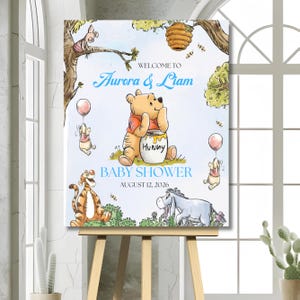Może przedstawiać: Prostokątny znak powitalny na baby shower z postaciami z Kubusia Puchatka, w tym Prosiaczkiem, Tygryskiem i Kłapouchym. Tekst brzmi Welcome to Aurora & Liam Baby Shower August 12, 2026. Puchatek siedzi na środku z garnkiem miodu z napisem Hunny.