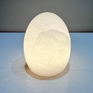 May include: A glowing, egg-shaped lamp with a textured surface. The lamp emits a soft, warm light, creating a serene ambiance. The egg-shaped lamp is a decorative lighting element, perfect for a bedroom or living room.