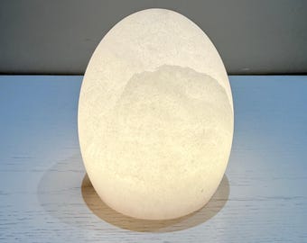 May include: A glowing, egg-shaped lamp with a textured surface. The lamp emits a soft, warm light, creating a serene ambiance. The egg-shaped lamp is a decorative lighting element, perfect for a bedroom or living room.
