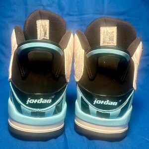May include: Pair of high-top Jordan sneakers. The shoes feature a black and light blue color scheme with the word "Jordan" printed on the heel. The uppers are black with light blue accents and a white patterned design on the sides.