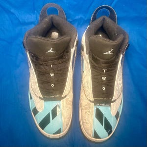May include: Pair of high-top sneakers with a black and white design, featuring a light blue accent on the toe and side panels. The sneakers have the word "TWO" and the brand name "JORDAN" visible.
