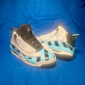May include: Pair of high-top sneakers in a light blue, black, and white color scheme. The sneakers feature a patterned design on the upper, with black stripes and accents. The soles are white and black, with a visible air cushion.